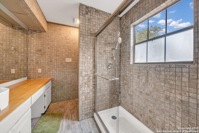 bathroom with a shower with door, vanity, hardwood / wood-style flooring, and tile walls