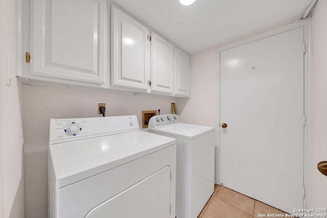 clothes washing area featuring separate washer and dryer, light tile patterned floors, and cabinets