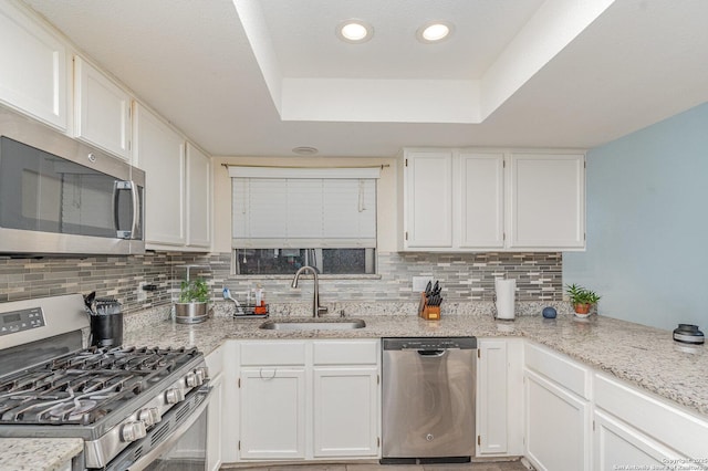 kitchen with sink, appliances with stainless steel finishes, a tray ceiling, light stone countertops, and white cabinets