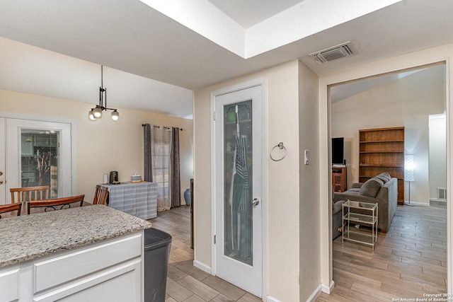 kitchen with vaulted ceiling, white cabinetry, light stone countertops, and decorative light fixtures