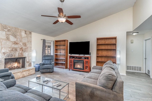 living room with a stone fireplace, high vaulted ceiling, a textured ceiling, ceiling fan, and light hardwood / wood-style floors