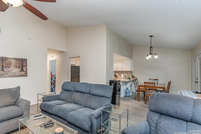 living room with vaulted ceiling, ceiling fan with notable chandelier, and light hardwood / wood-style floors