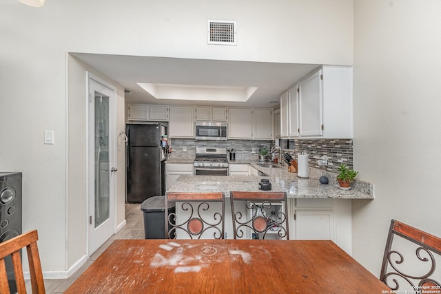 kitchen featuring appliances with stainless steel finishes, sink, decorative backsplash, kitchen peninsula, and a raised ceiling