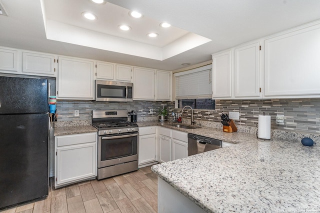 kitchen featuring white cabinetry, appliances with stainless steel finishes, backsplash, and a tray ceiling