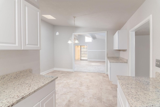 kitchen with pendant lighting, light stone counters, white cabinets, light carpet, and vaulted ceiling