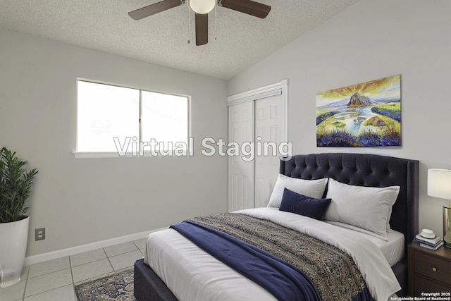 tiled bedroom with ceiling fan, vaulted ceiling, a closet, and a textured ceiling