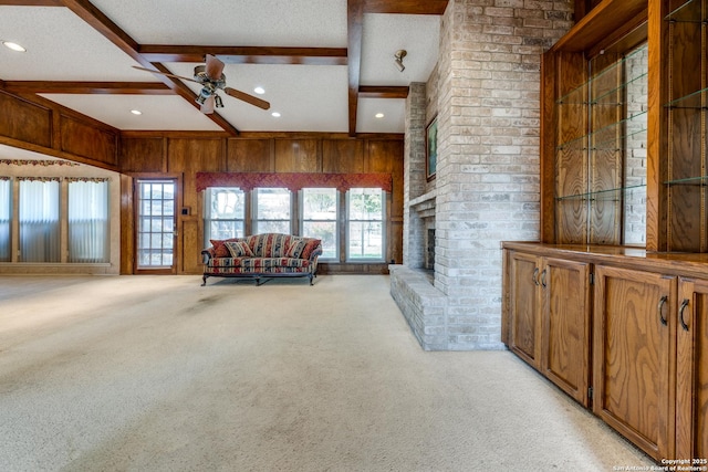 living room with beam ceiling, light carpet, wooden walls, ceiling fan, and a fireplace