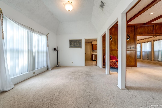 empty room featuring a healthy amount of sunlight, vaulted ceiling with beams, light carpet, and a textured ceiling