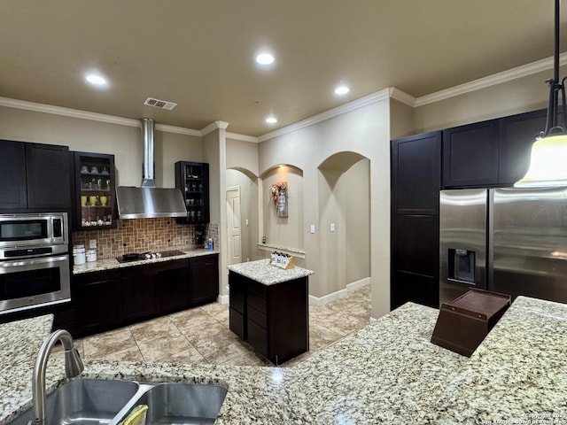 kitchen with wall chimney range hood, sink, appliances with stainless steel finishes, a center island, and decorative backsplash