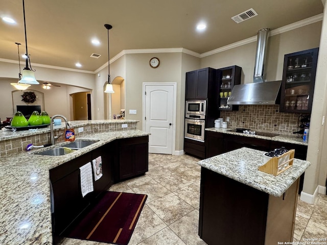 kitchen featuring wall chimney exhaust hood, sink, decorative light fixtures, a center island, and appliances with stainless steel finishes