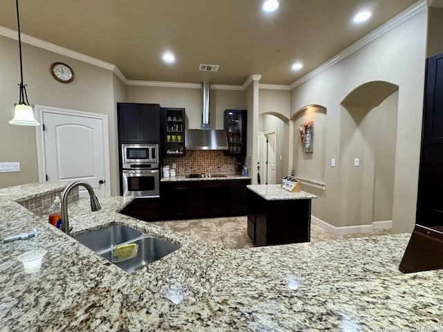 kitchen with appliances with stainless steel finishes, a kitchen island, sink, light stone countertops, and wall chimney exhaust hood