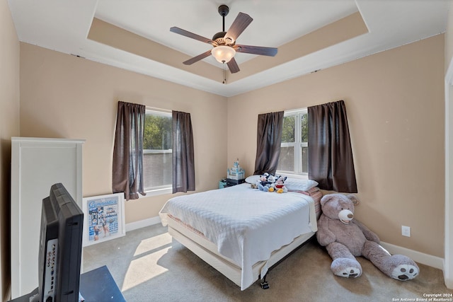 carpeted bedroom with ceiling fan, a raised ceiling, and multiple windows