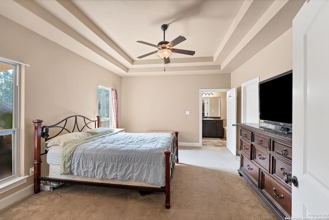 carpeted bedroom with ceiling fan, ensuite bathroom, a raised ceiling, and multiple windows