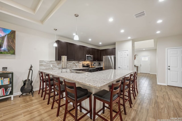 kitchen featuring appliances with stainless steel finishes, hanging light fixtures, backsplash, dark brown cabinets, and kitchen peninsula