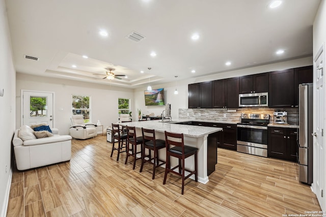 kitchen with pendant lighting, a breakfast bar area, stainless steel appliances, light stone counters, and a raised ceiling