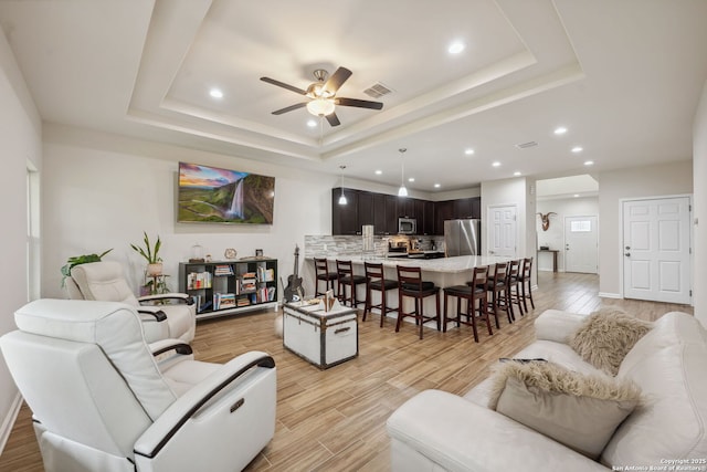 living room with a tray ceiling, light hardwood / wood-style flooring, and ceiling fan