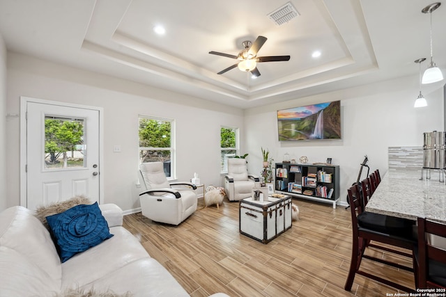 living room with ceiling fan, a raised ceiling, and light hardwood / wood-style floors