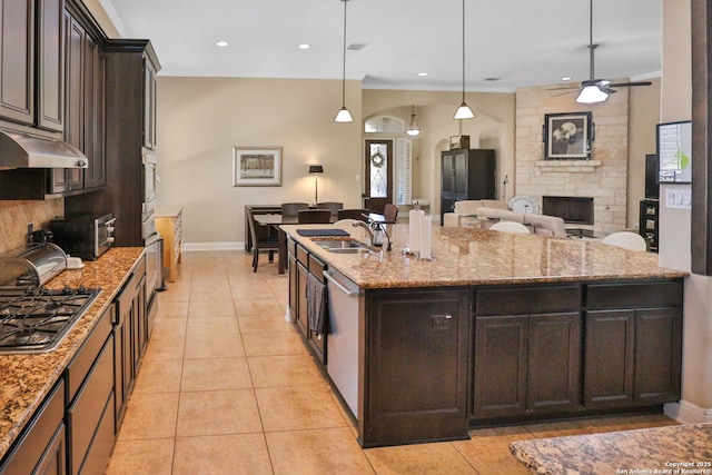 kitchen with sink, hanging light fixtures, stainless steel appliances, light stone counters, and a center island with sink