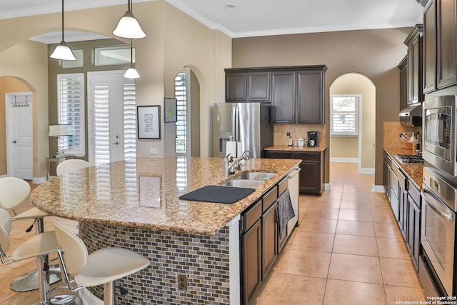 kitchen with decorative light fixtures, sink, light tile patterned floors, stainless steel appliances, and a center island with sink