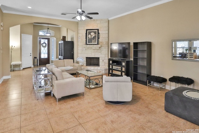 living room featuring crown molding, ceiling fan, a stone fireplace, and light tile patterned floors