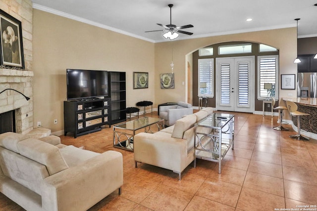 tiled living room with ornamental molding, a stone fireplace, ceiling fan, and french doors