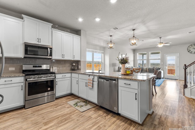 kitchen with white cabinetry, appliances with stainless steel finishes, decorative light fixtures, and kitchen peninsula