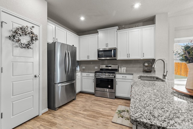 kitchen featuring sink, light wood-type flooring, stainless steel appliances, light stone countertops, and white cabinets