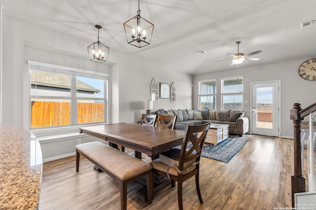 dining space featuring hardwood / wood-style flooring, ceiling fan with notable chandelier, and a textured ceiling