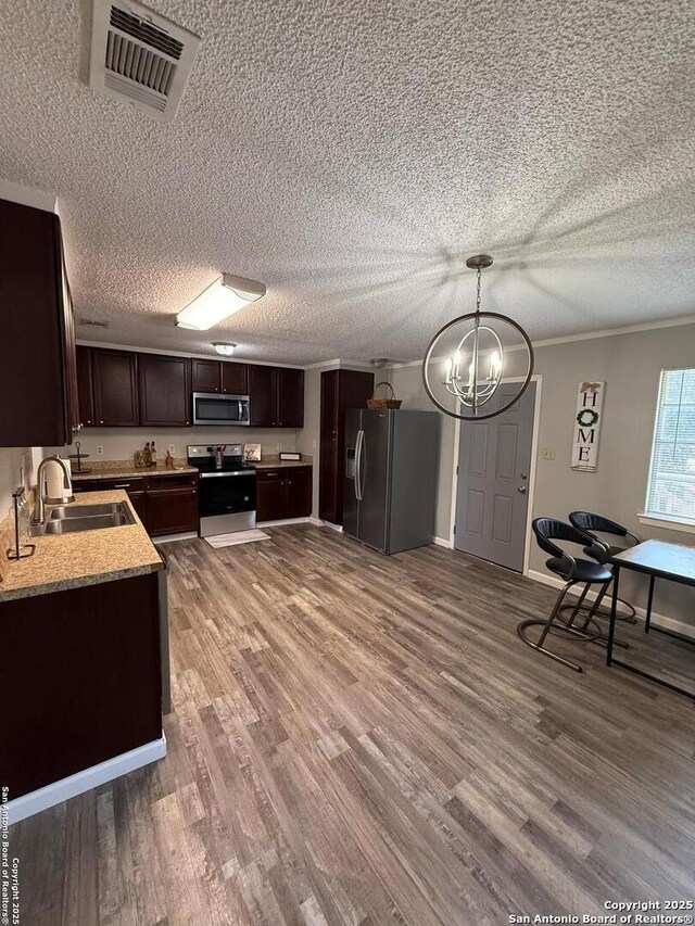 kitchen with sink, appliances with stainless steel finishes, dark brown cabinetry, wood-type flooring, and decorative light fixtures