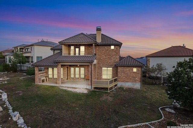 back house at dusk featuring a lawn and a patio