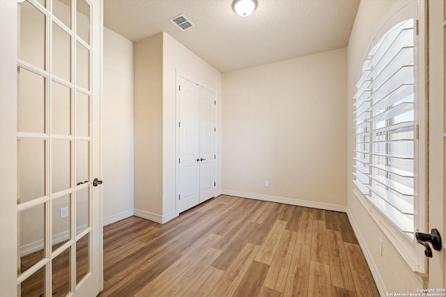 unfurnished bedroom with light hardwood / wood-style flooring, french doors, and a textured ceiling