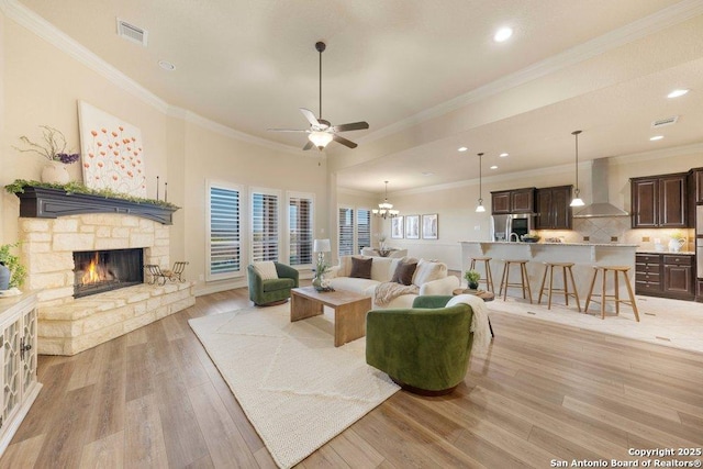 living room featuring a fireplace, light wood-type flooring, crown molding, and ceiling fan with notable chandelier