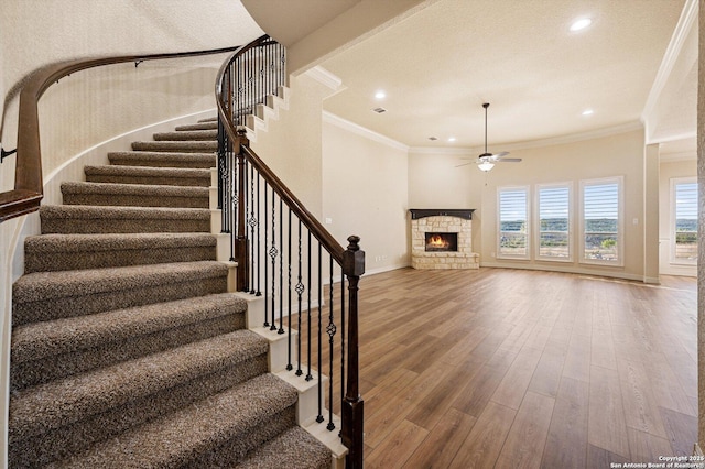 staircase with hardwood / wood-style flooring, ceiling fan, ornamental molding, and a fireplace