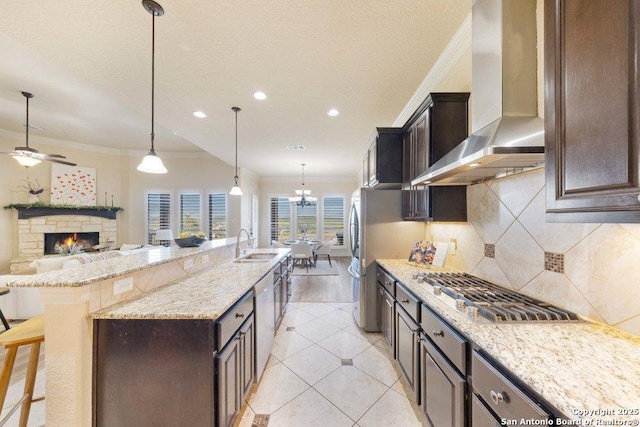 kitchen with a breakfast bar, sink, ornamental molding, wall chimney exhaust hood, and pendant lighting