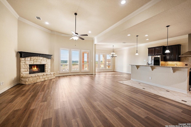 unfurnished living room featuring a textured ceiling, dark hardwood / wood-style floors, ceiling fan with notable chandelier, crown molding, and a fireplace