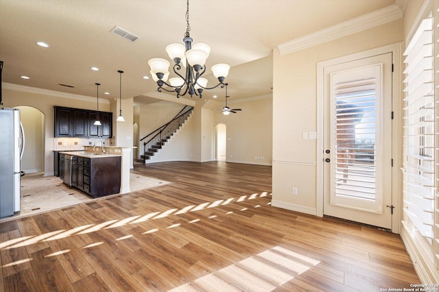 kitchen featuring hanging light fixtures, dark brown cabinetry, crown molding, stainless steel fridge, and sink