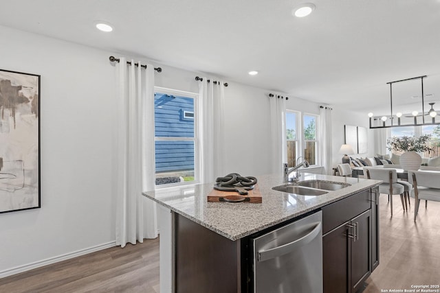 kitchen featuring sink, dishwasher, dark brown cabinets, light stone countertops, and a center island with sink