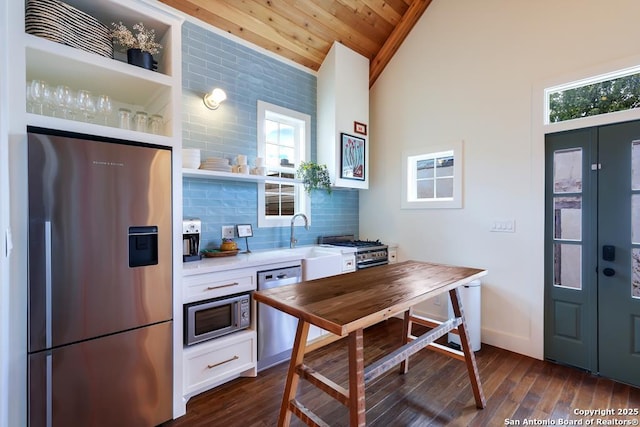 kitchen with vaulted ceiling, dark hardwood / wood-style flooring, white cabinets, stainless steel appliances, and backsplash