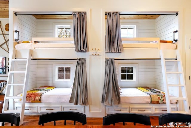 bedroom with multiple windows, wood-type flooring, and wood walls