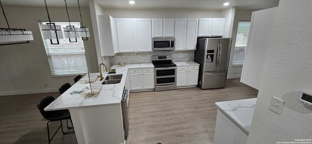 kitchen with appliances with stainless steel finishes, decorative light fixtures, sink, white cabinets, and a kitchen breakfast bar