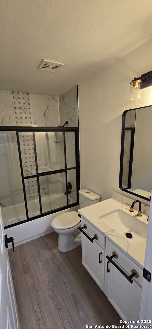 full bathroom with wood-type flooring, bath / shower combo with glass door, vanity, and a textured ceiling