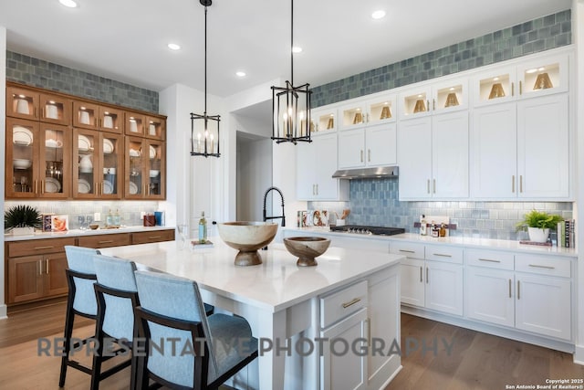 kitchen with dark hardwood / wood-style floors, a center island with sink, white cabinets, and decorative light fixtures