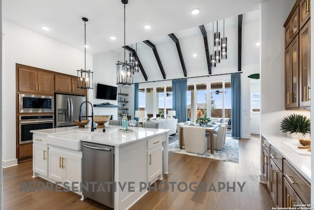 kitchen featuring pendant lighting, stainless steel appliances, a kitchen island with sink, and white cabinets