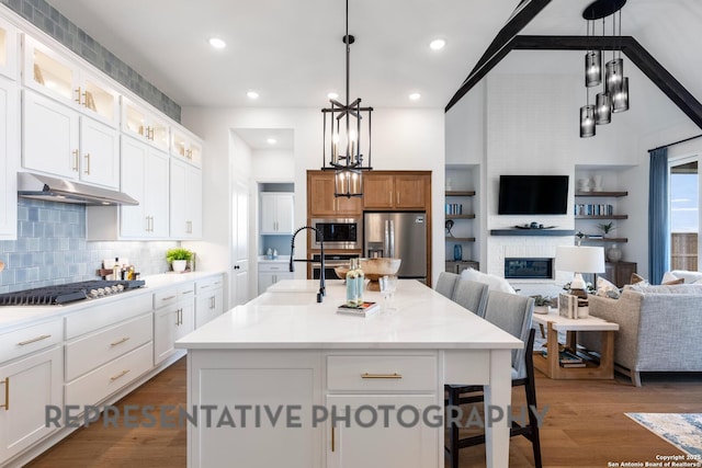 kitchen with white cabinetry, appliances with stainless steel finishes, hanging light fixtures, and a center island with sink