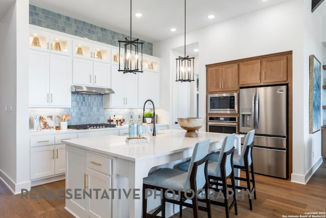 kitchen with white cabinetry, stainless steel appliances, and a center island with sink