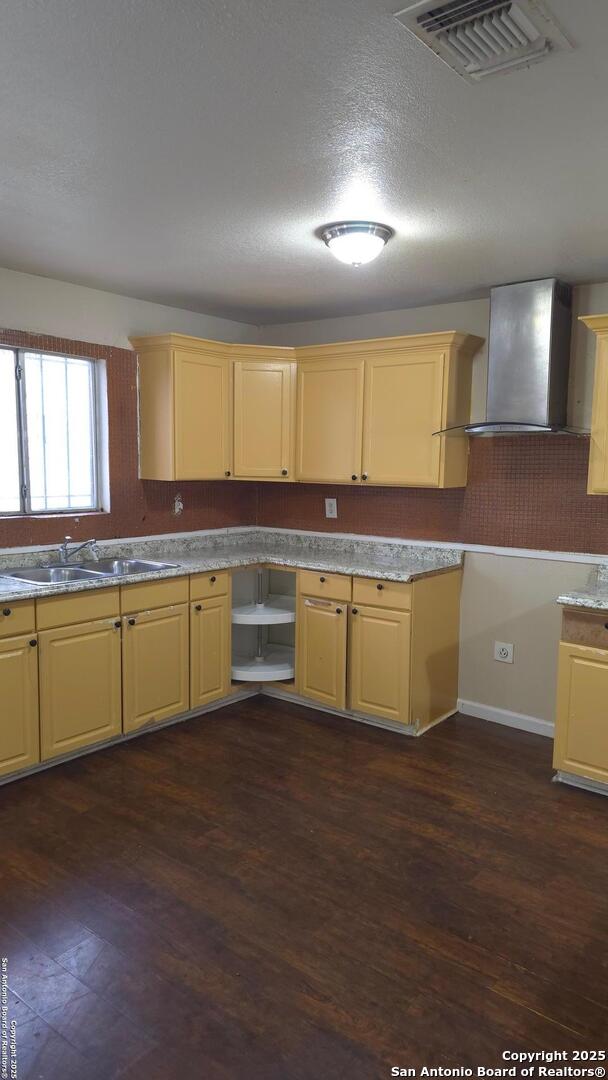 kitchen with sink, wall chimney range hood, a textured ceiling, and dark wood-type flooring