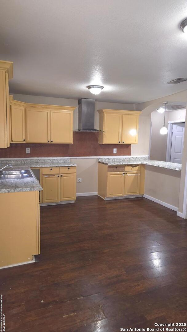 kitchen with light brown cabinetry, sink, hanging light fixtures, dark hardwood / wood-style flooring, and wall chimney range hood