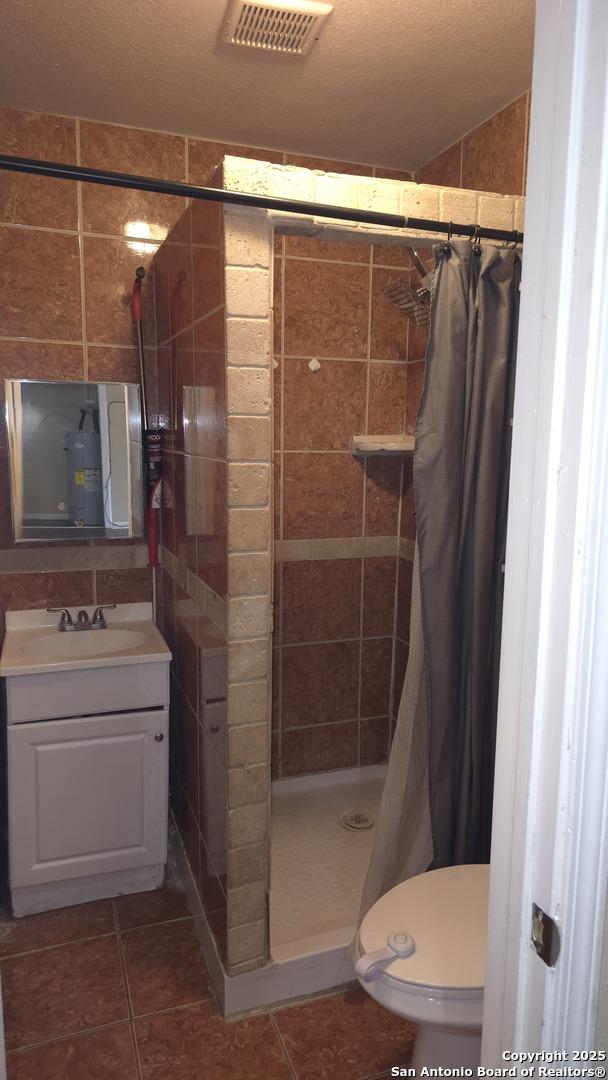 bathroom featuring walk in shower, toilet, a textured ceiling, vanity, and tile patterned flooring