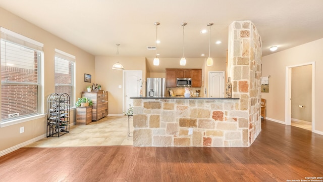 kitchen featuring decorative light fixtures, stainless steel appliances, light hardwood / wood-style floors, and kitchen peninsula