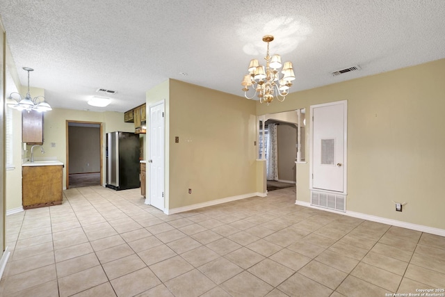 empty room featuring a notable chandelier, light tile patterned floors, sink, and a textured ceiling